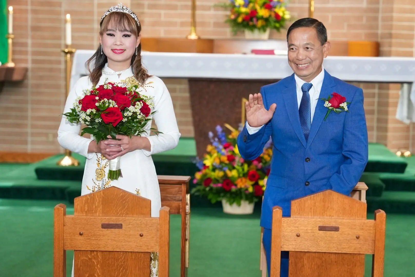 A man and woman standing in front of pews holding flowers.